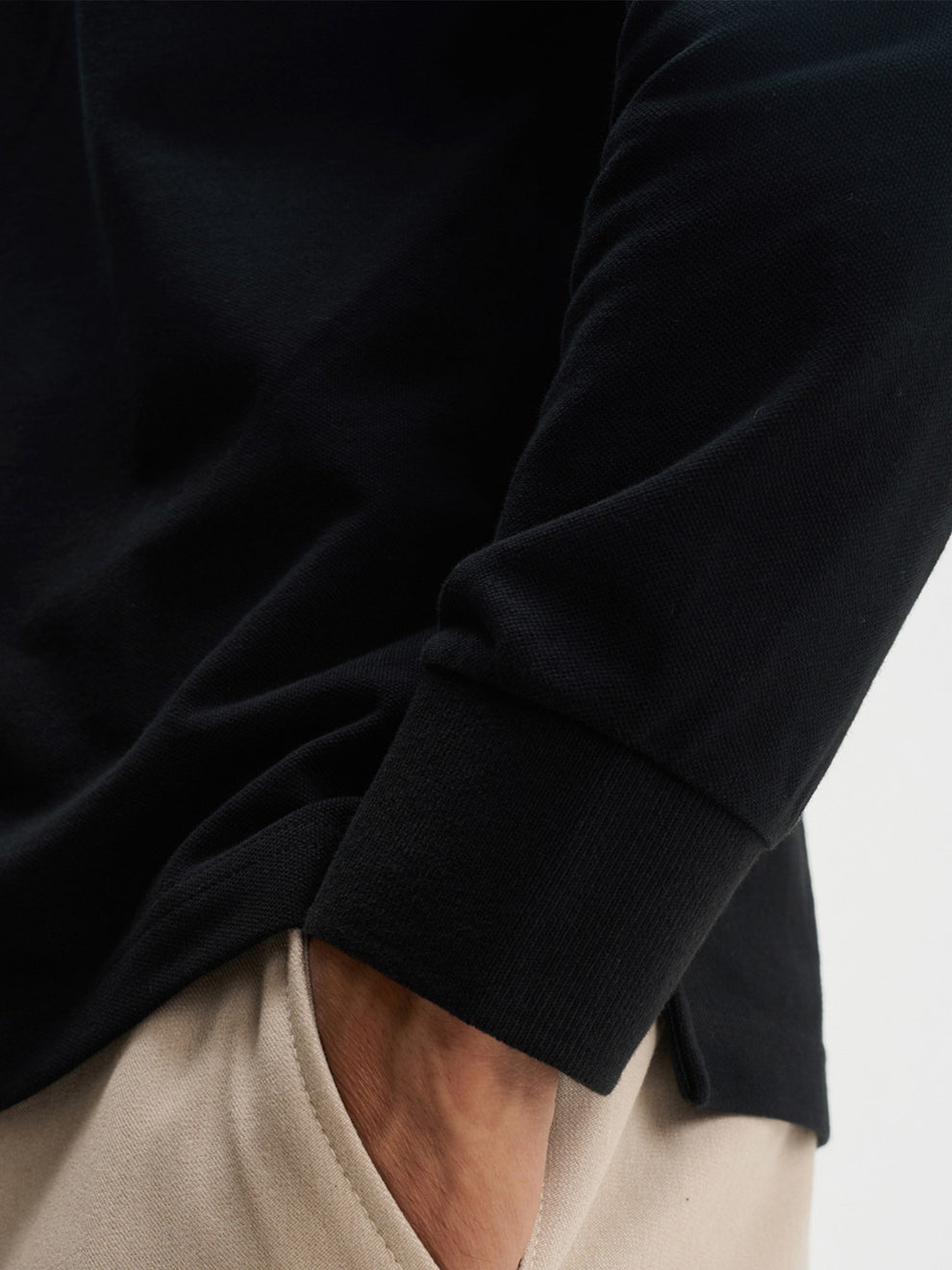 Person wearing a black long-sleeve shirt with beige pants on a light gray background