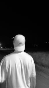 Person wearing a white cap and shirt walking away on a dark road at night.