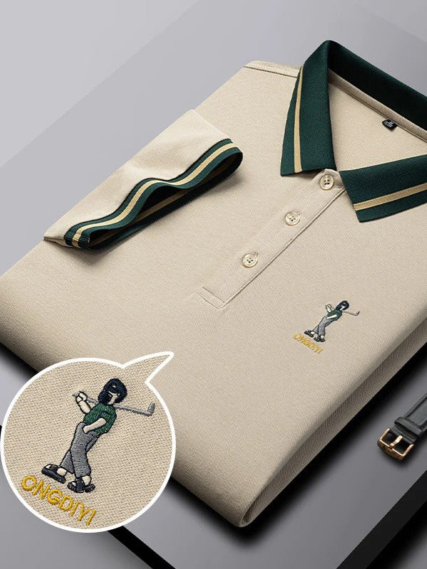 Beige polo shirt with green trim and embroidered design on a gray surface