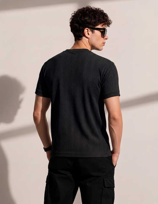 Man wearing a black t-shirt and sunglasses against a beige wall