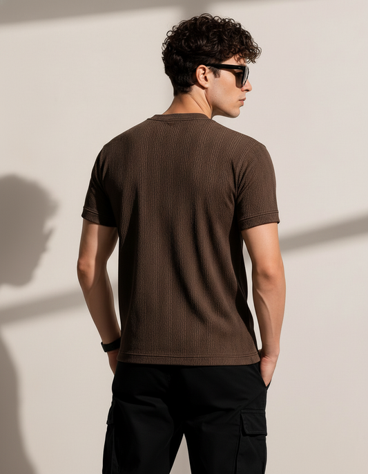 Man wearing a brown t-shirt and black sunglasses against a beige wall