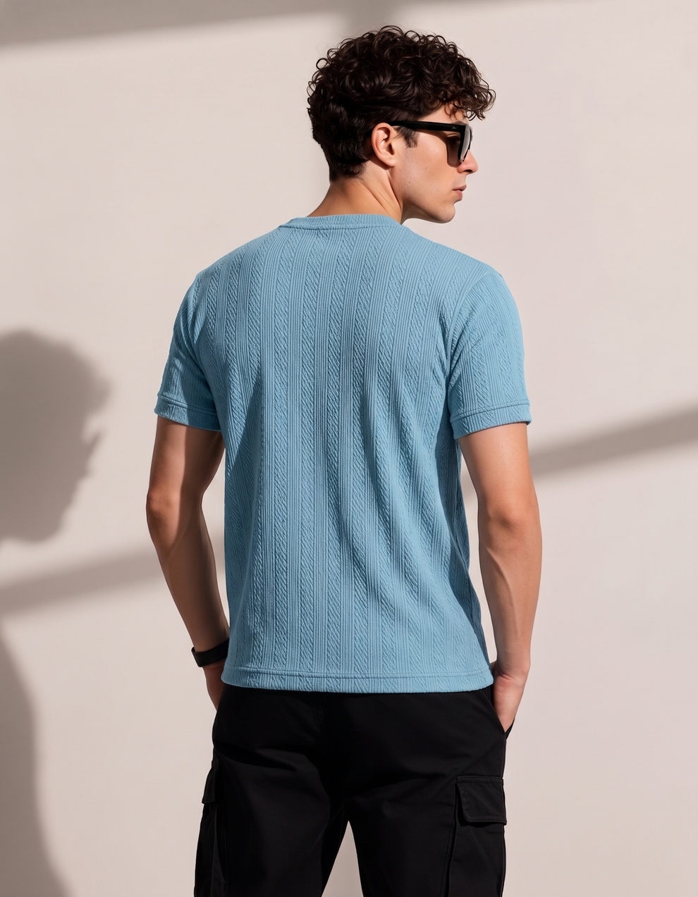 Man wearing a blue textured t-shirt against a beige wall