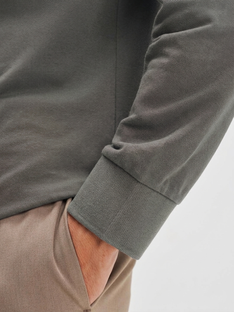 Close-up of a person wearing a gray long-sleeve shirt with beige pants on a light gray background