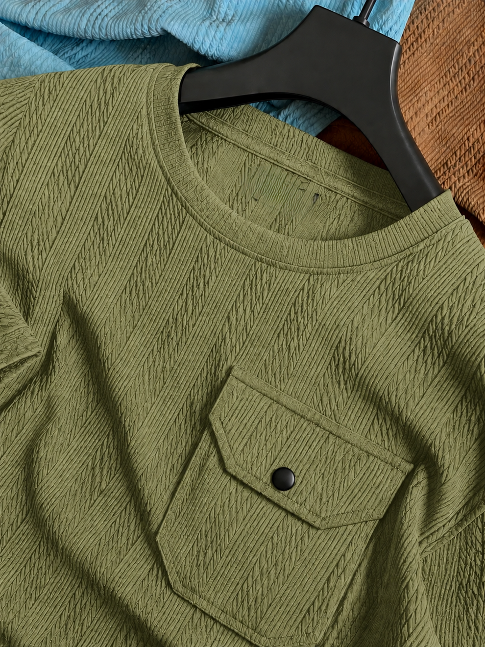 Green shirt with a pocket on a hanger against a blue fabric background
