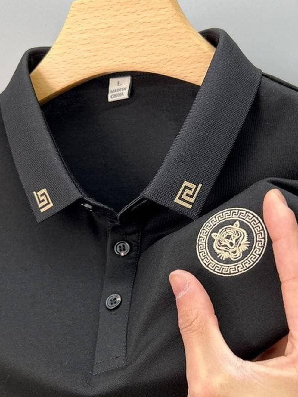Black polo shirt with a tiger emblem and brand logo on a hanger.
