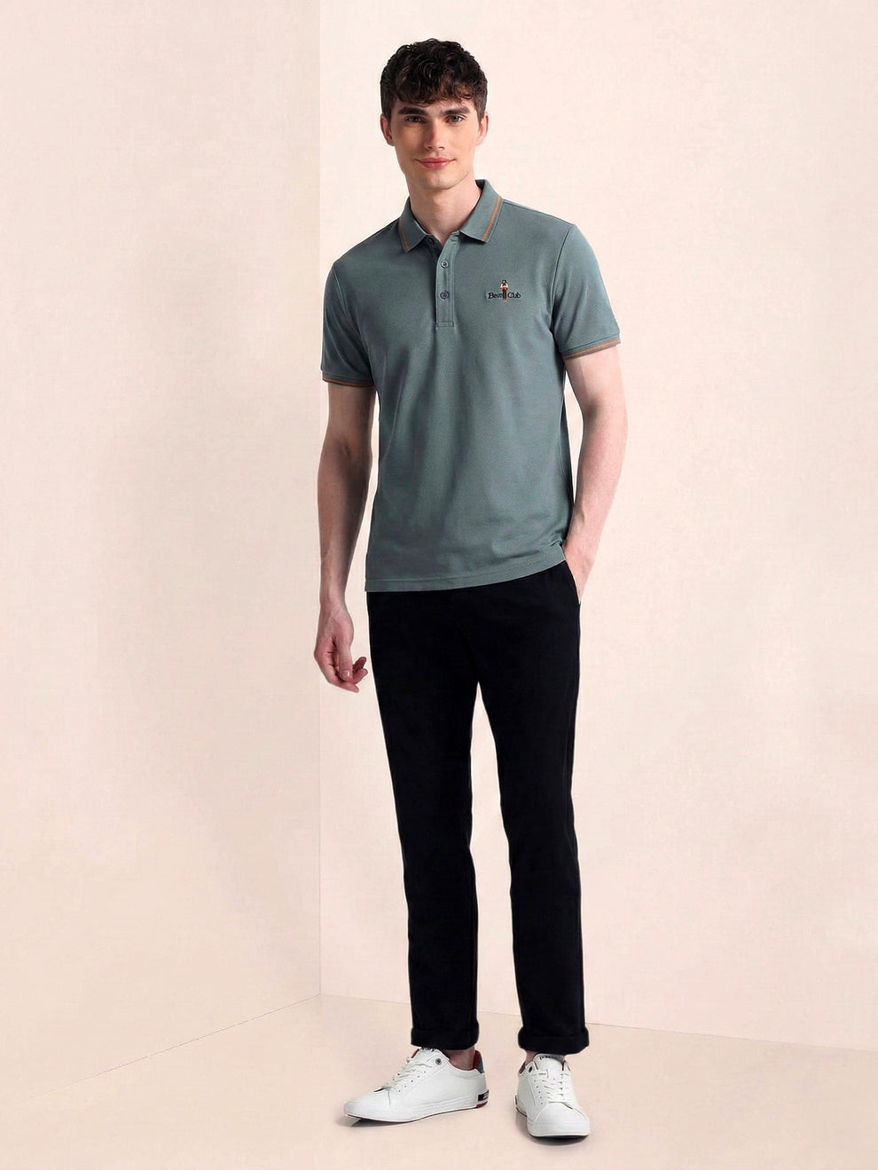 Man wearing a green polo shirt and black pants on a beige background
