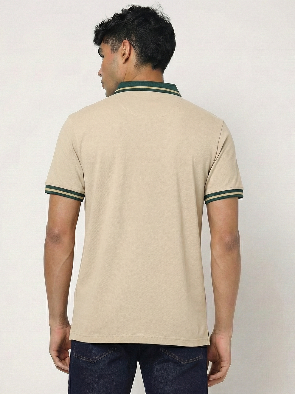 Man wearing a beige polo shirt with green trim on a plain background