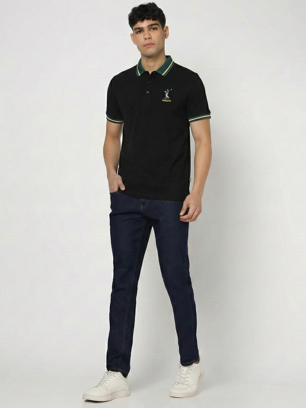 Man wearing a black polo shirt with a logo and dark jeans on a white background