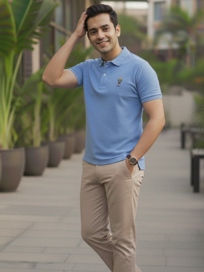Man wearing a blue polo shirt and beige pants standing outdoors with plants in the background