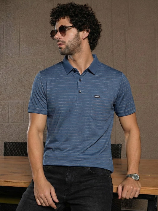 Man wearing a blue striped polo shirt sitting at a table with a neutral background