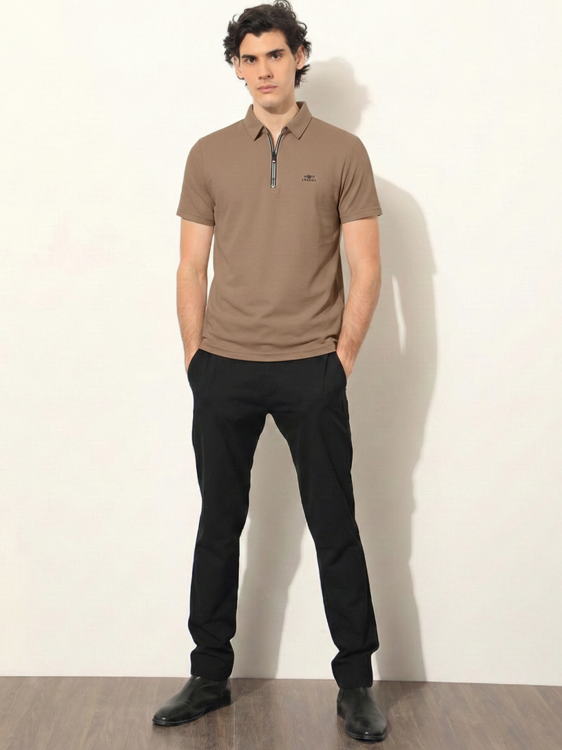 Man wearing a brown polo shirt and black pants against a white wall.