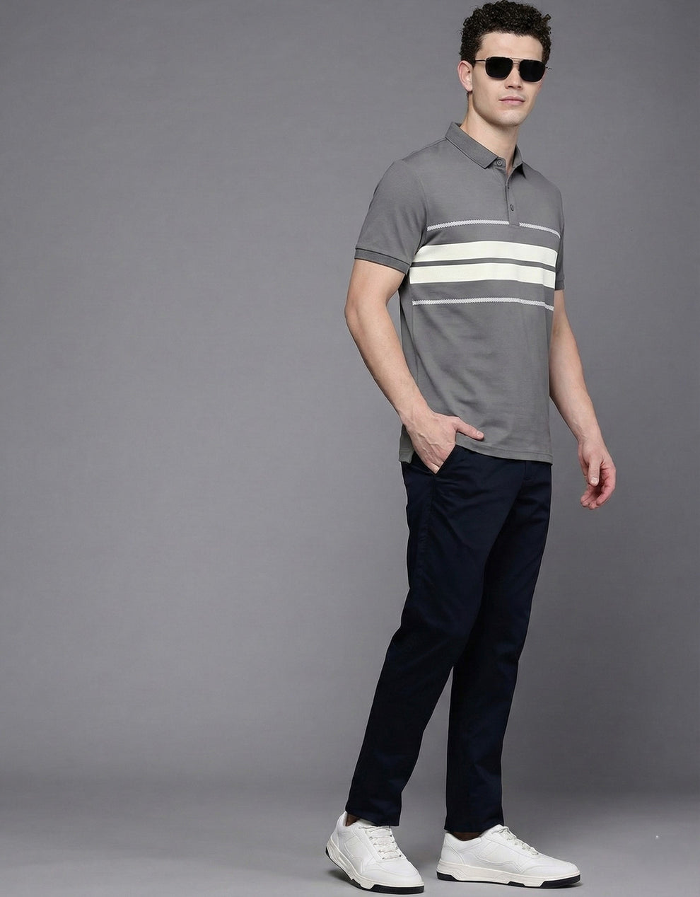 Man wearing a gray polo shirt with white stripes and dark pants on a gray background