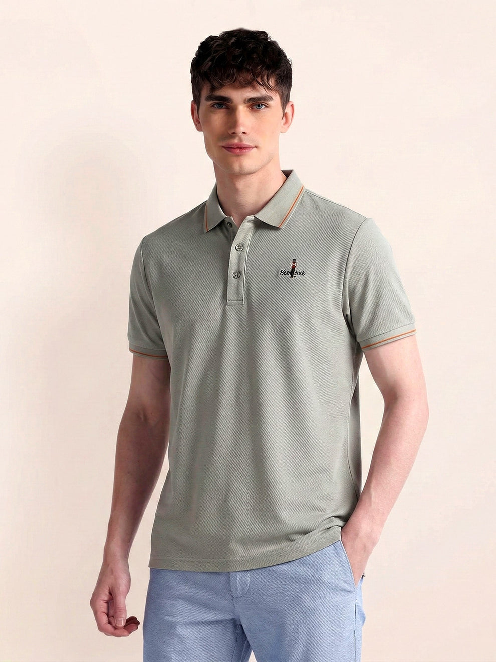 Man wearing a light green polo shirt with a small logo on a beige background