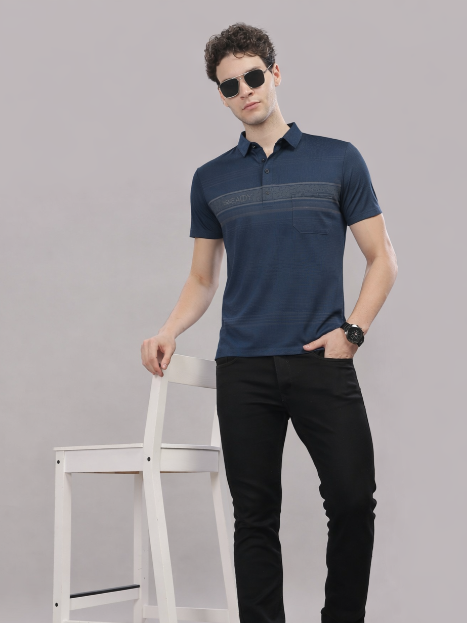 Man wearing a navy blue polo shirt and black pants standing against a gray background
