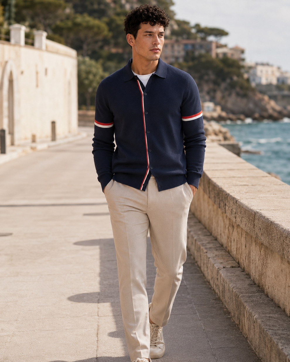 Man wearing a navy cardigan with red and white stripes, standing by a waterfront.