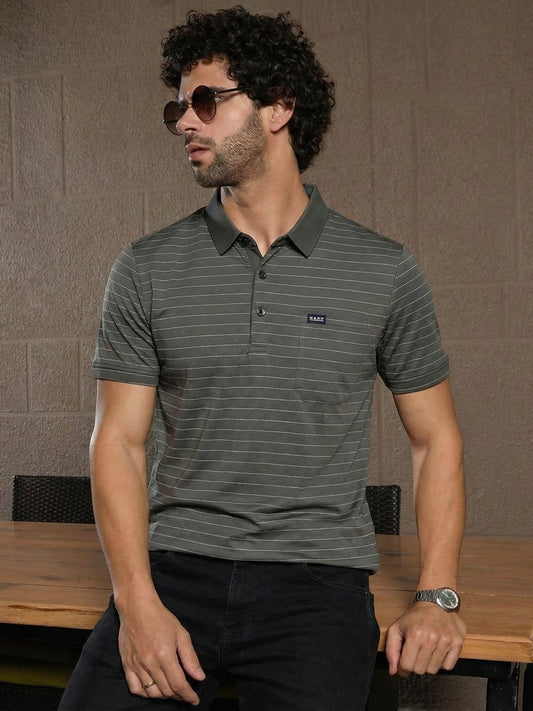 Man wearing a striped polo shirt with a brand logo, sitting at a table against a textured wall.