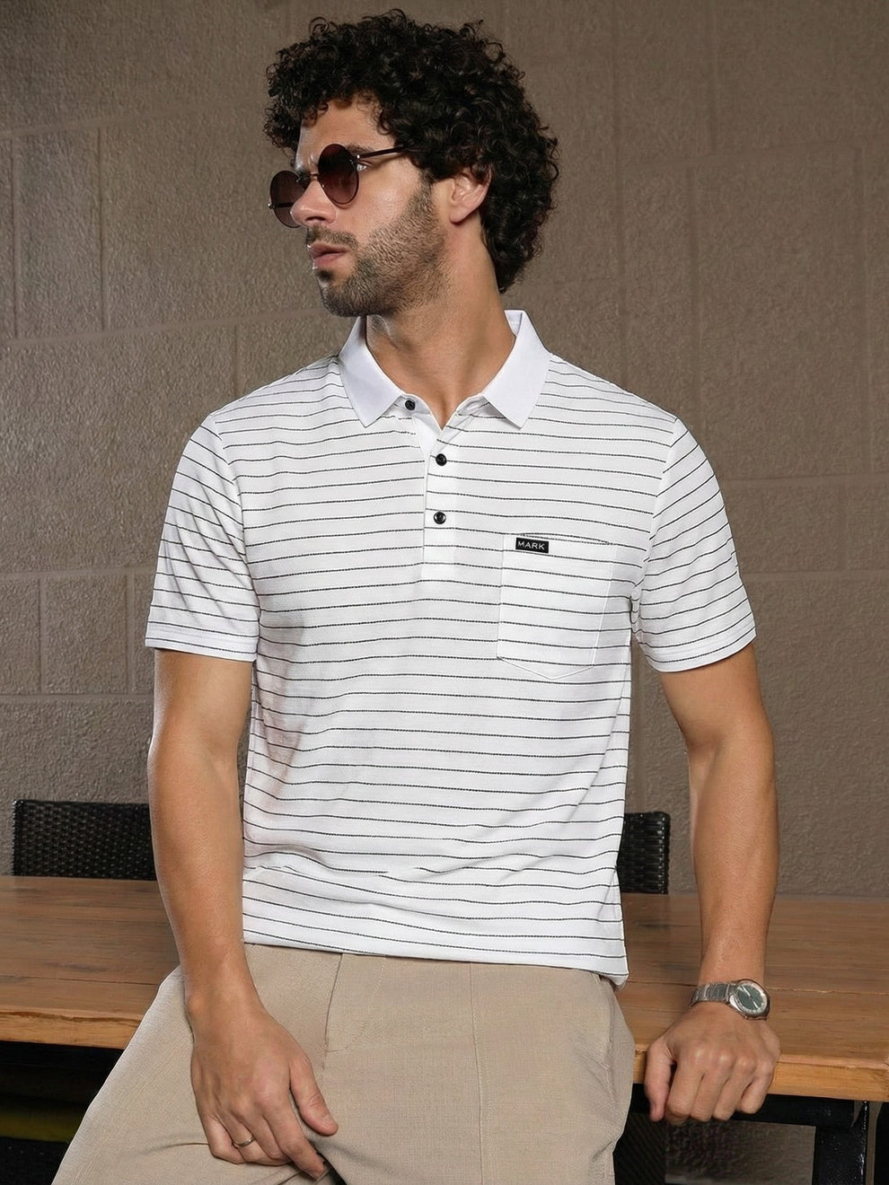 Man wearing a white striped polo shirt sitting at a table with a neutral background