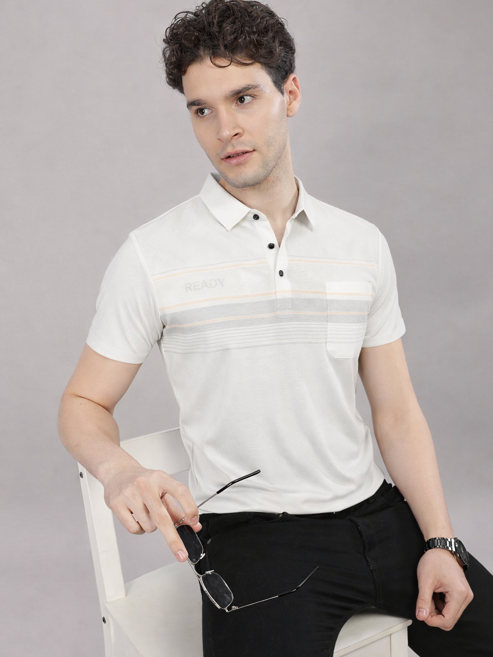 Man wearing a white striped polo shirt sitting on a chair against a gray background