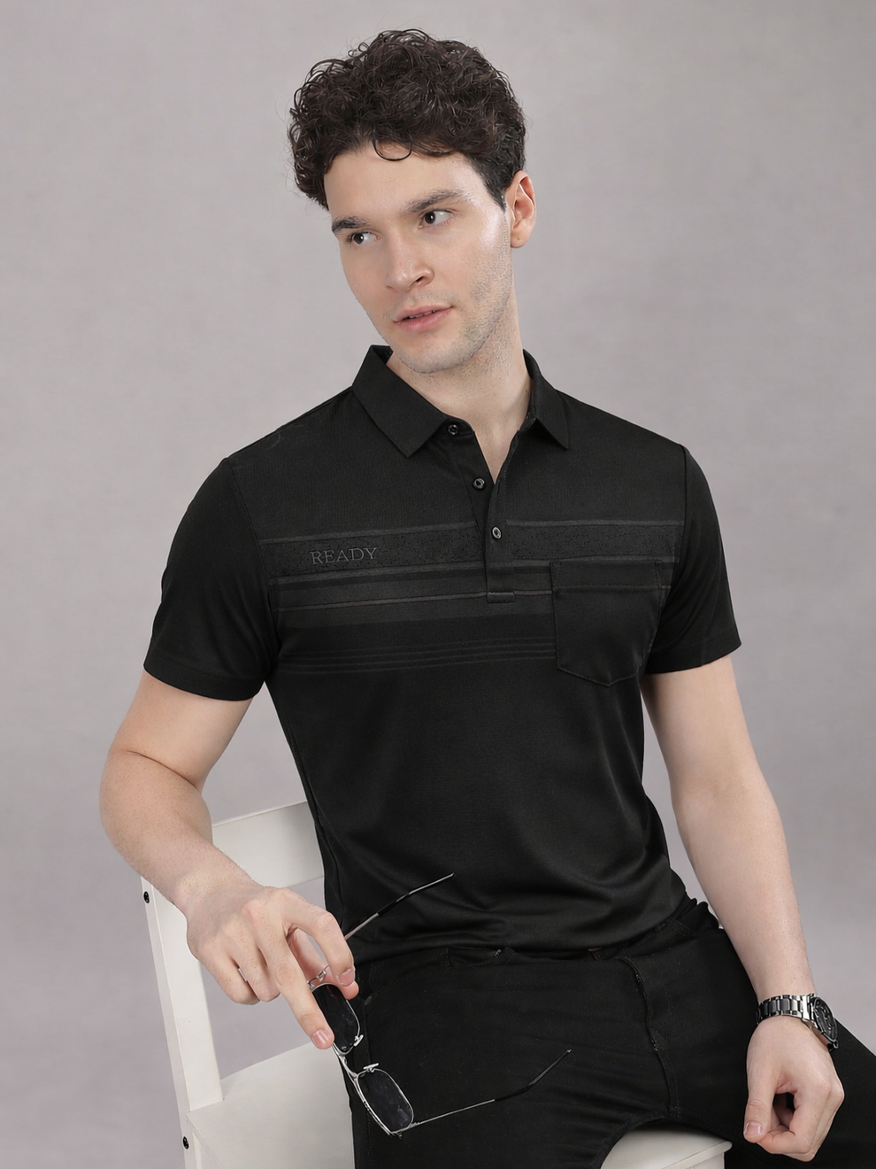 Man wearing a black polo shirt with a brand logo on a gray background