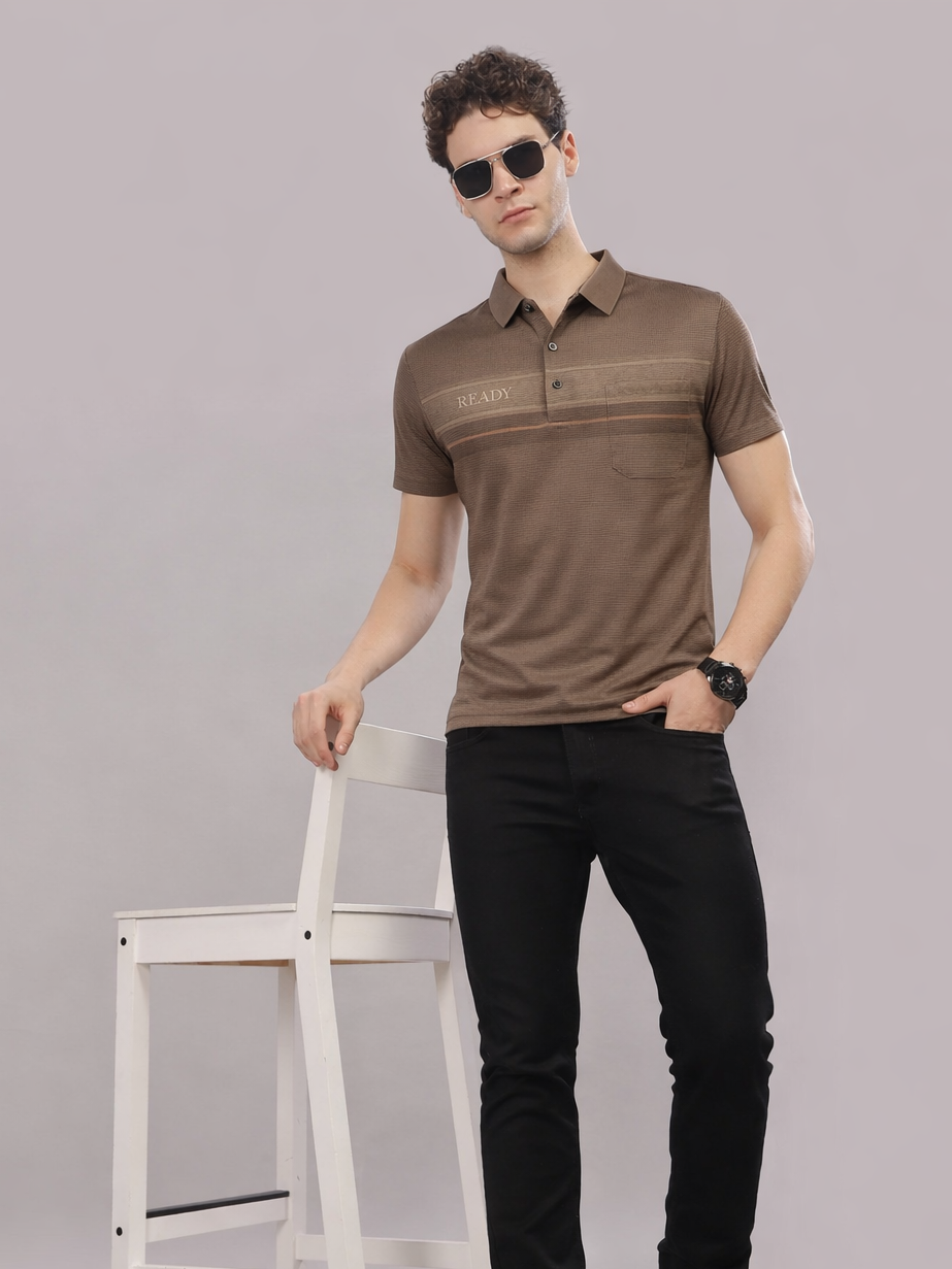 Man wearing a brown polo shirt and black pants against a gray background
