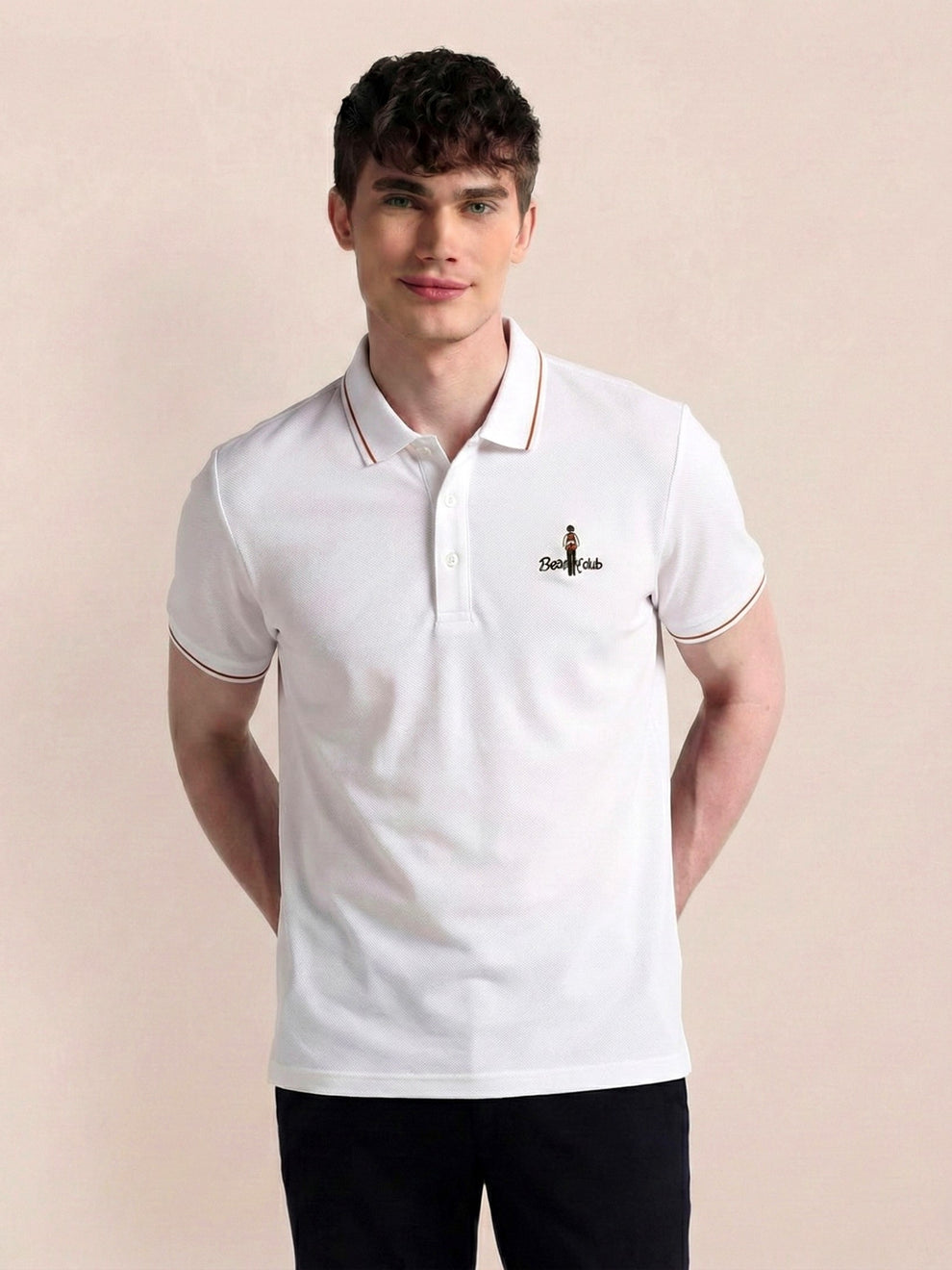 Man wearing a white polo shirt with a logo on a beige background
