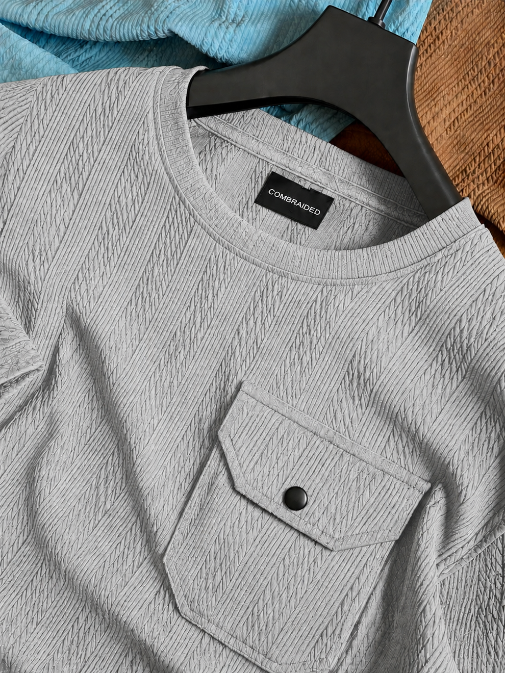 Gray shirt with a pocket and button on a hanger against a blue fabric background