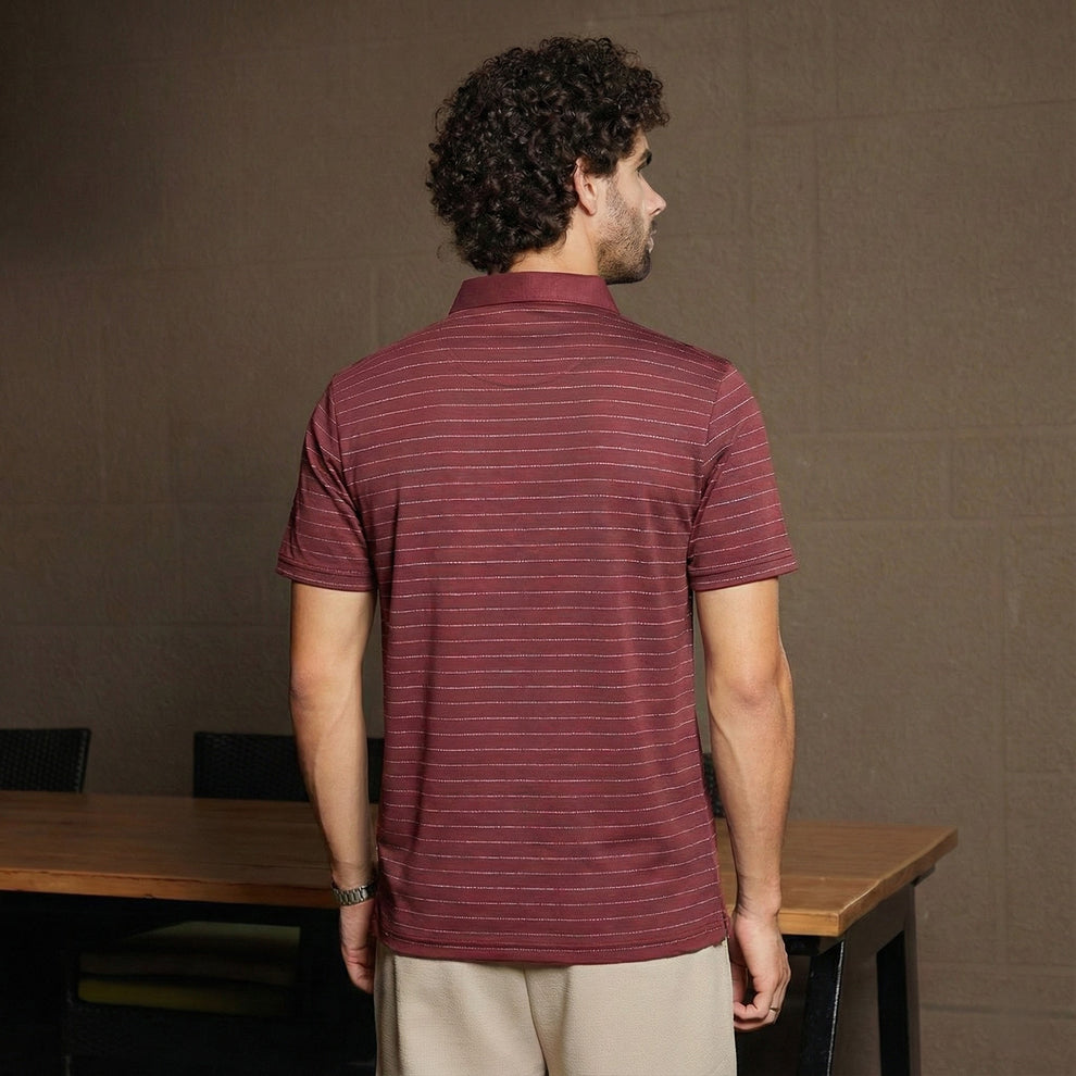 Man wearing a maroon striped polo shirt standing in front of a brown wall.