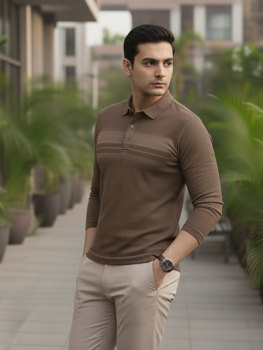 Man wearing a brown long-sleeve polo shirt and beige pants standing outdoors with plants and buildings in the background.