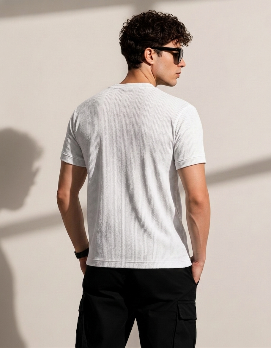 Man wearing a white t-shirt and black pants against a beige wall