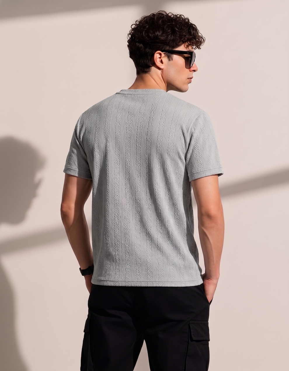 Man wearing a gray textured t-shirt and black sunglasses against a beige wall