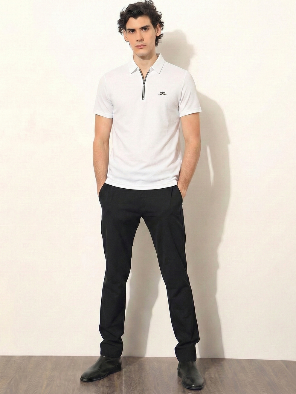 Man wearing a white polo shirt and black pants against a plain background