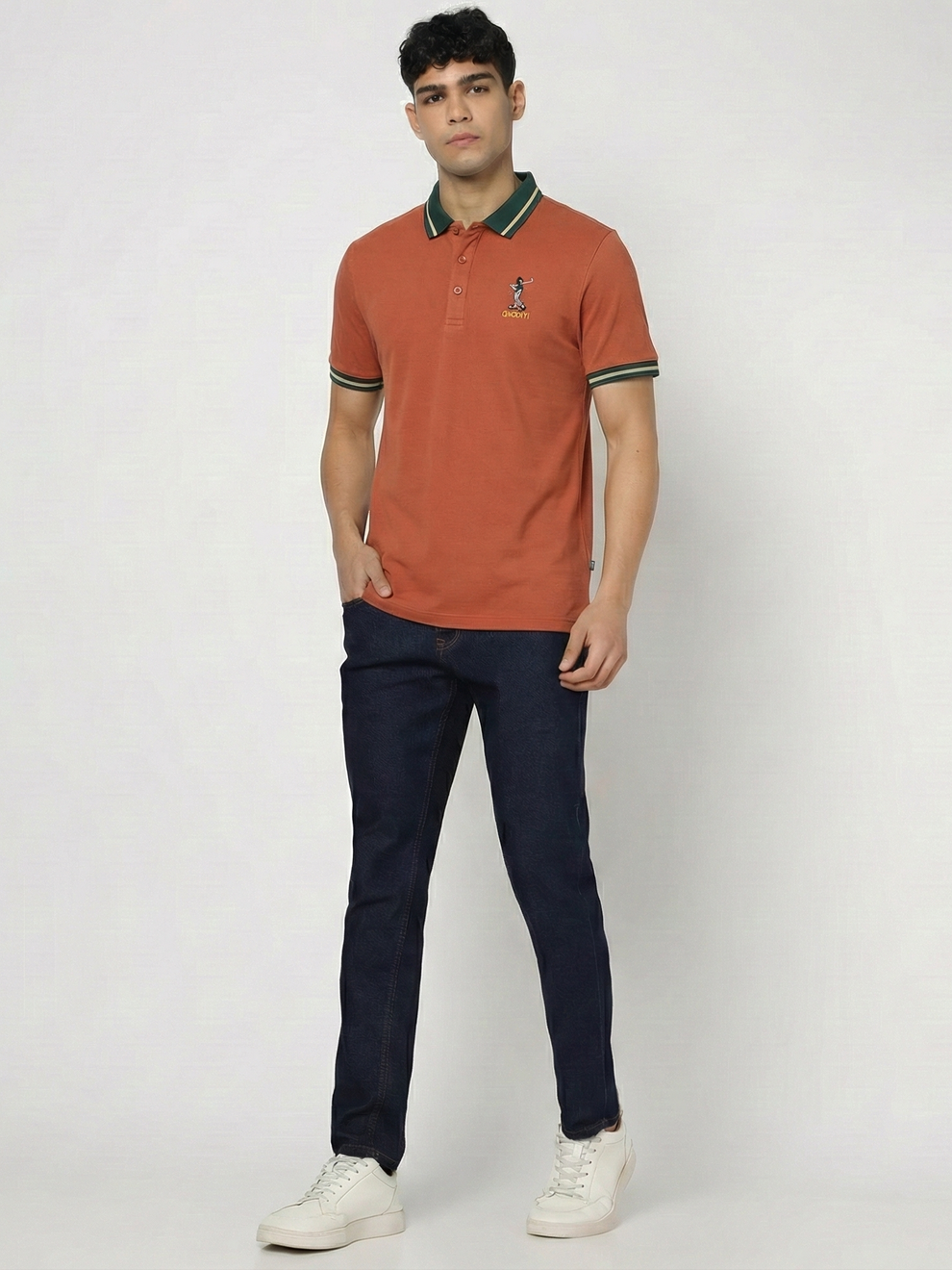 Man wearing a Orange polo shirt with green trim and dark jeans on a white background