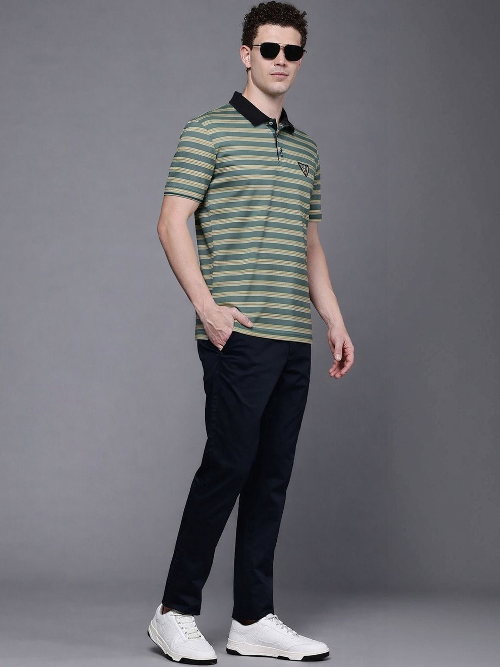 Man wearing a green and black striped polo shirt with black pants on a gray background