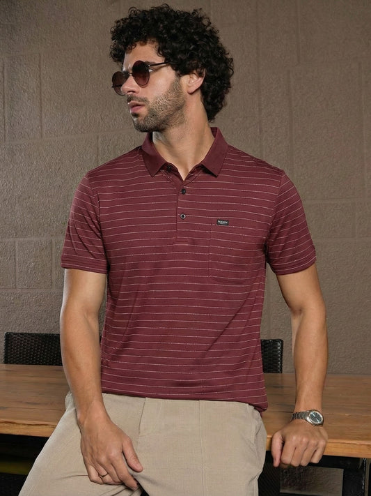 Man wearing a maroon striped polo shirt sitting at a table with a neutral background