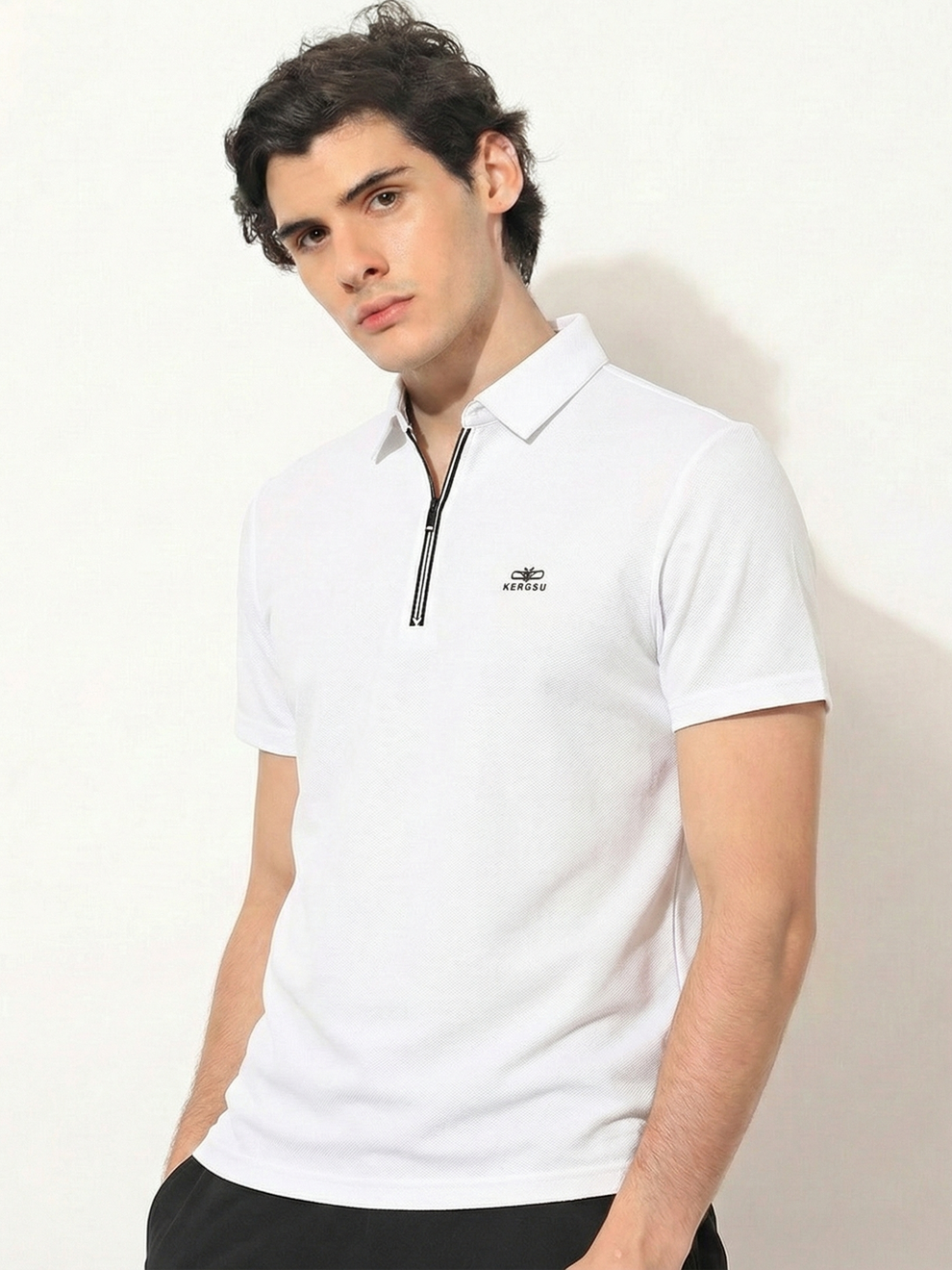 Man wearing a white polo shirt with a small logo on a plain background