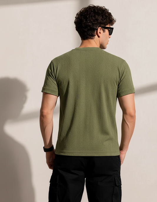 Man wearing a green t-shirt and black pants against a plain background