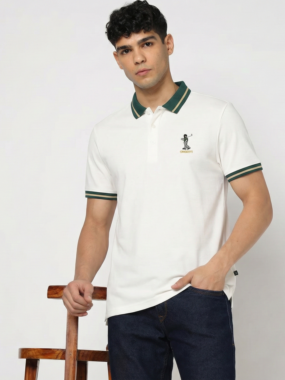Man wearing a white polo shirt with green accents and dark pants against a plain background