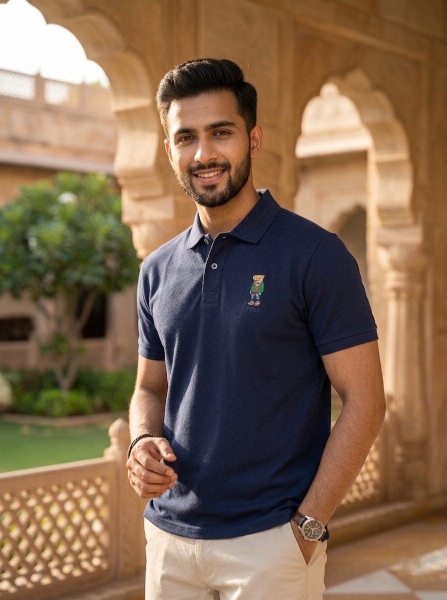 Man wearing a navy blue polo shirt with a logo, standing in front of an architectural background.