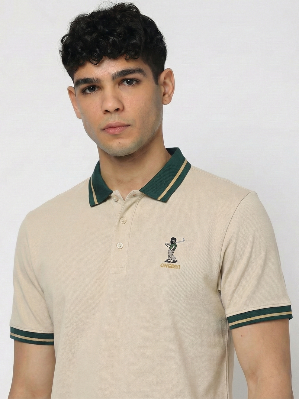 Man wearing a beige polo shirt with green accents and a logo on a plain background