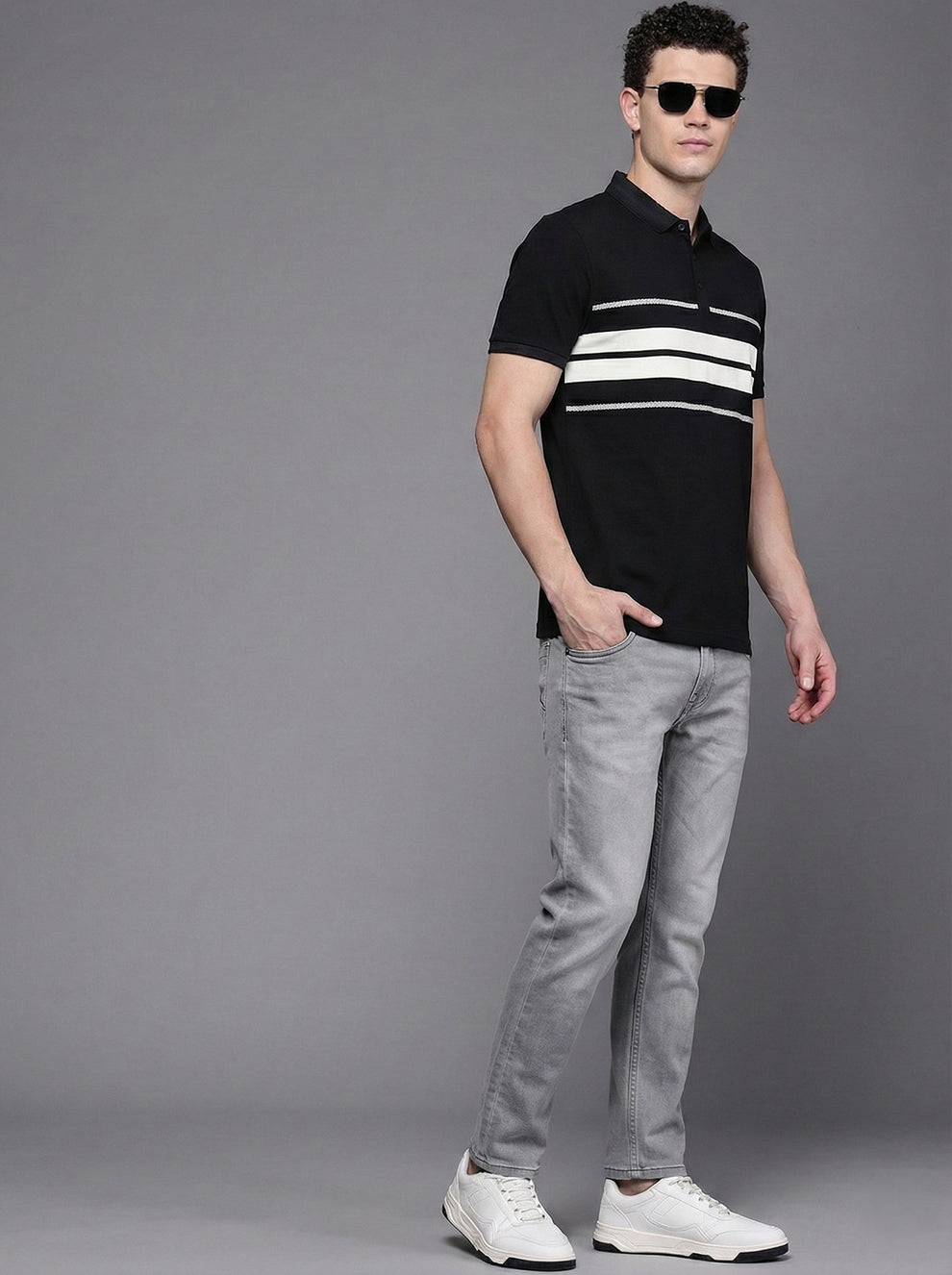 Man wearing a black and white striped polo shirt and gray pants on a gray background