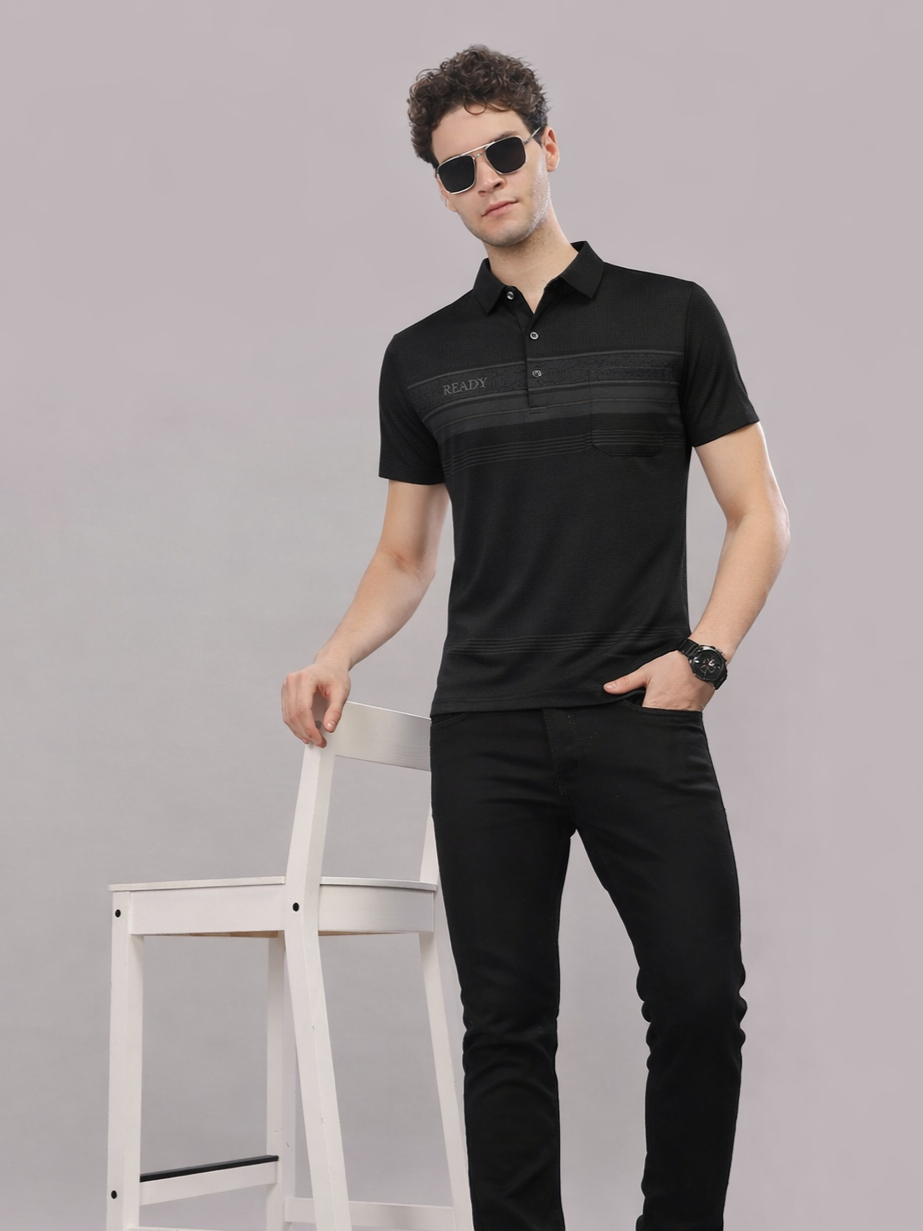 Man wearing a black polo shirt with a brand logo, standing against a gray background.