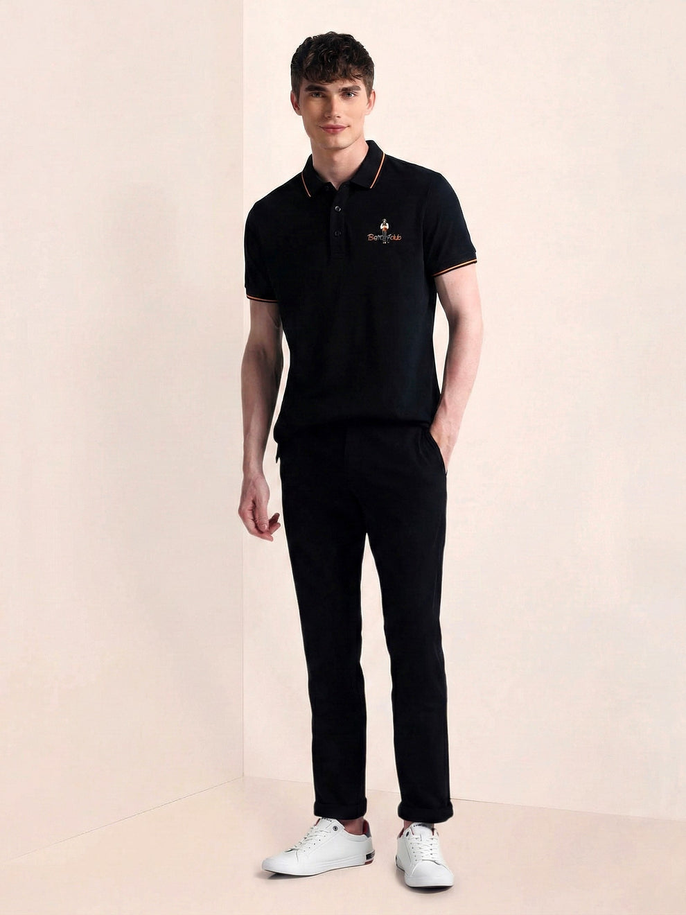 Man wearing a black polo shirt and pants with a logo on a beige background