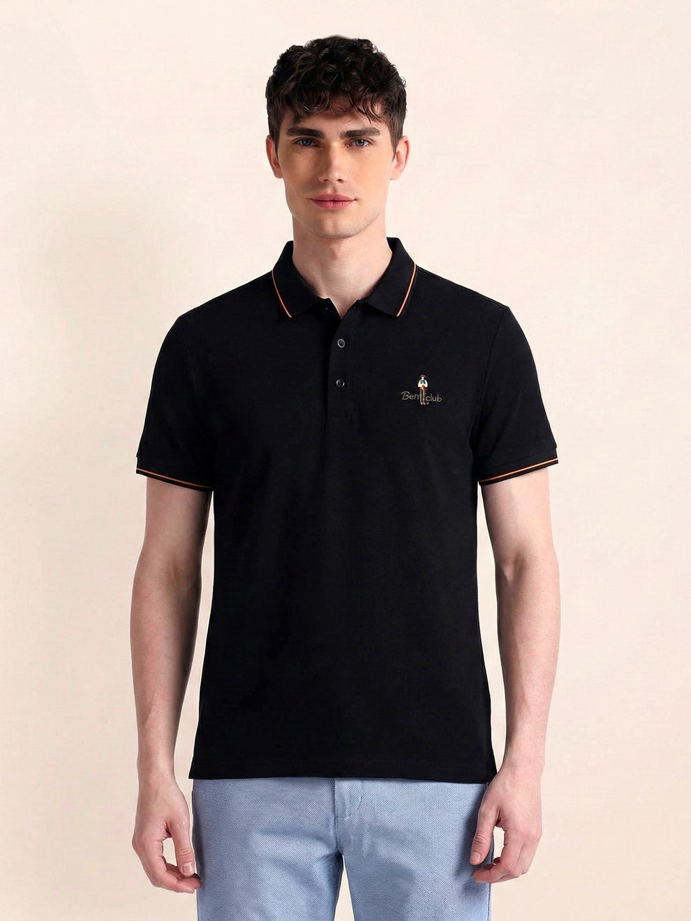 Man wearing a black polo shirt with a small logo on a beige background