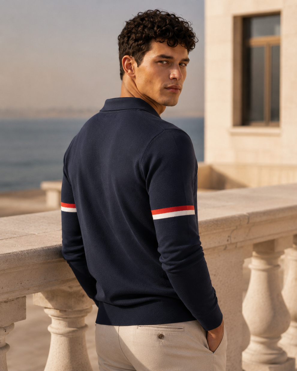 Man wearing a navy blue shirt with red and white stripes by a coastal building.