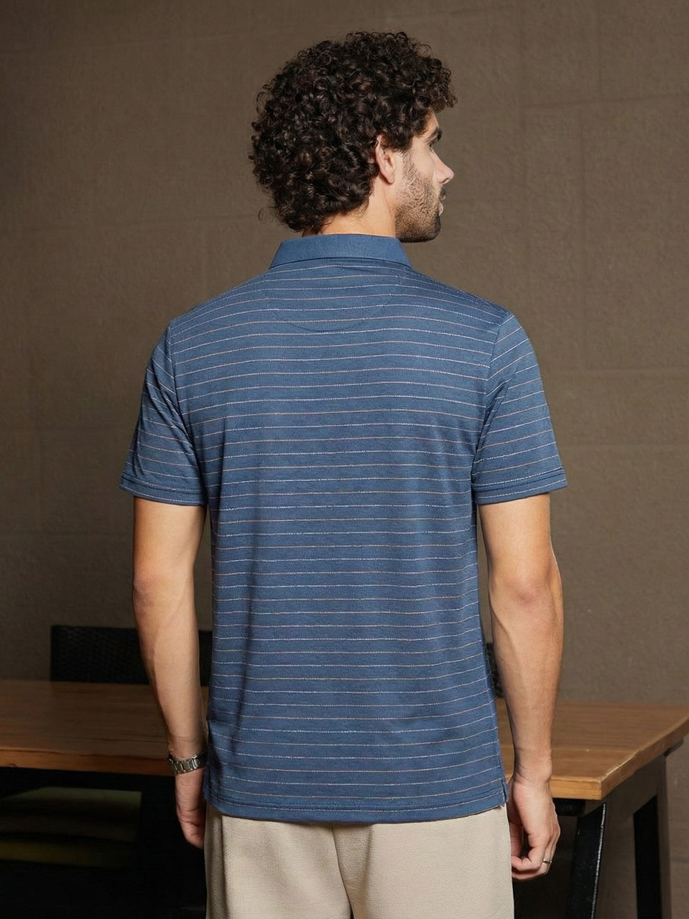 Man wearing a blue striped polo shirt standing in front of a brown wall.