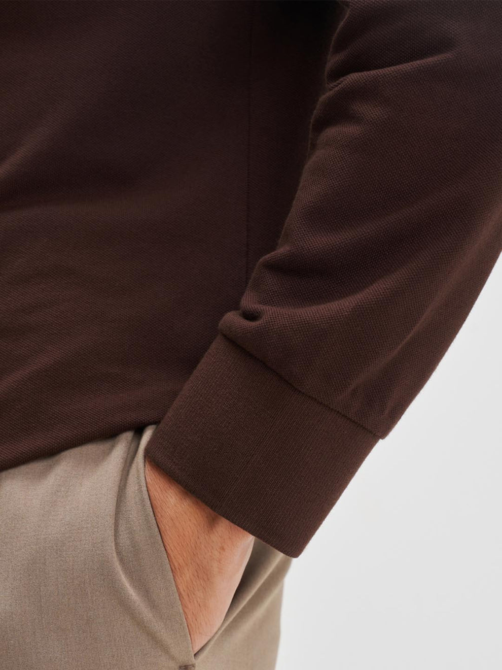 Close-up of a person wearing a brown long-sleeve shirt with a neutral background