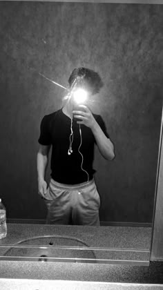 Person taking a mirror selfie with a light source, wearing a black t-shirt and beige pants.