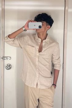 Person taking a mirror selfie wearing a beige shirt and light-colored pants.