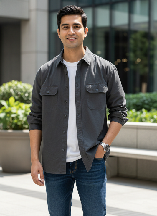 Man wearing a dark gray shirt over a white t-shirt, standing outdoors with plants and a building in the background.