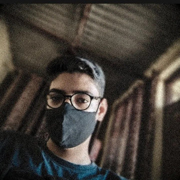 Person wearing a face mask and cap in a dimly lit room
